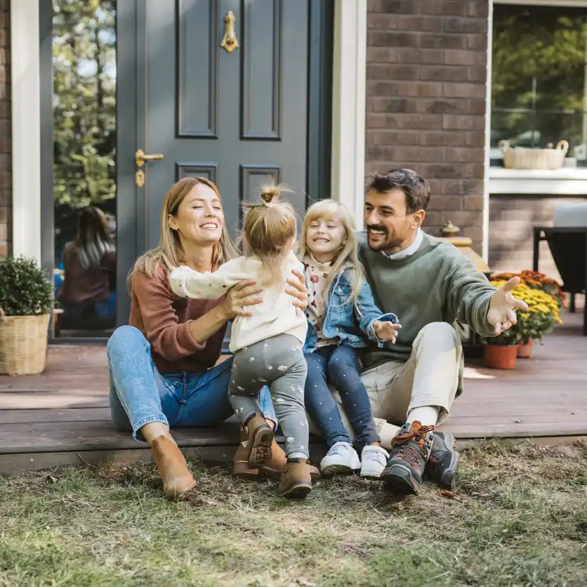 Happy family of four at doorstep of home, having family hug.