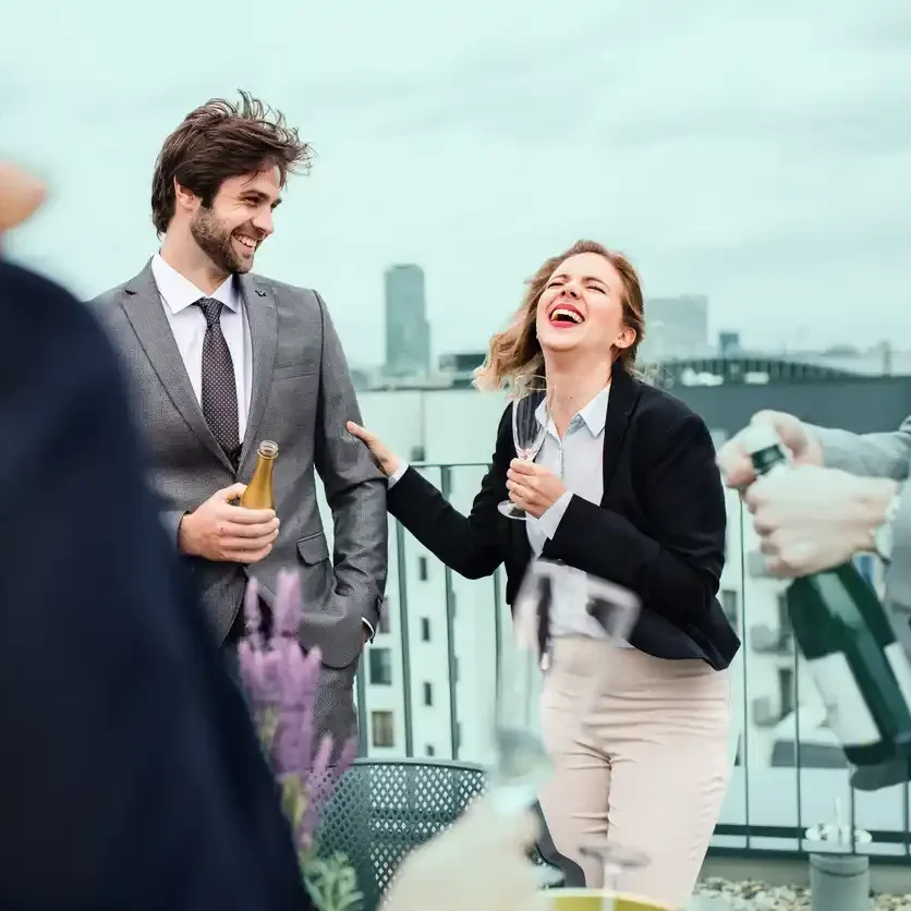 Copywriters laughing on rooftop bar in Perth with champagne in hand.