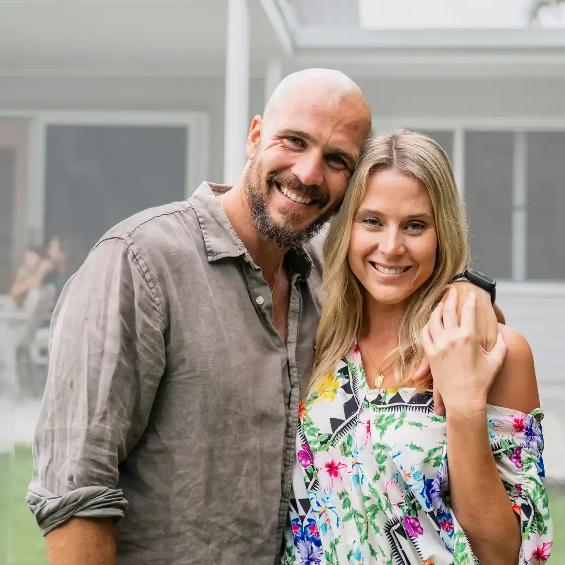 Grounded looking couple with arms around one another portraying the perfect family real estate customers in front of their affluent style home.