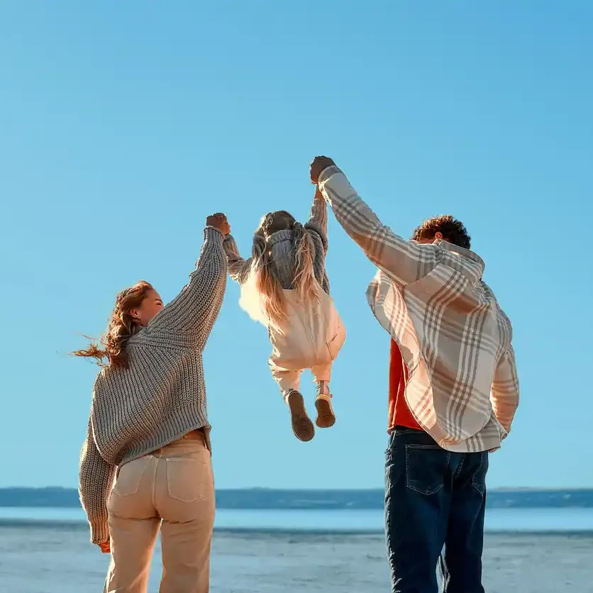Couple holding up their young son on a beach with light blue background filter.