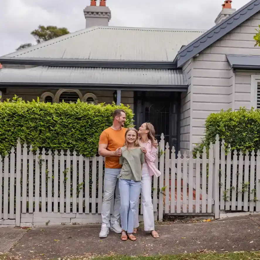 Happy couple with young daughter in front of newly purchased suburban home.