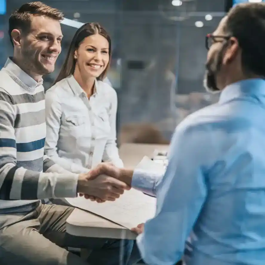 Real estate copywriter shaking hands with young business couple in office. 