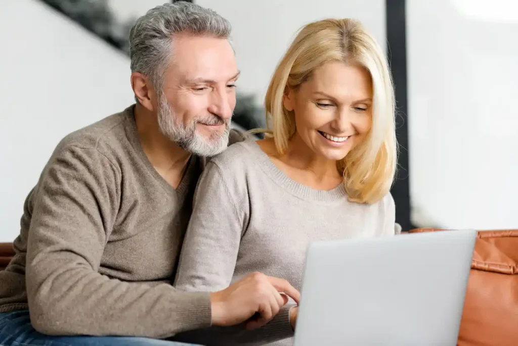 Mature couple smiling on couch with laptop in front of them feature mortgage broker website.