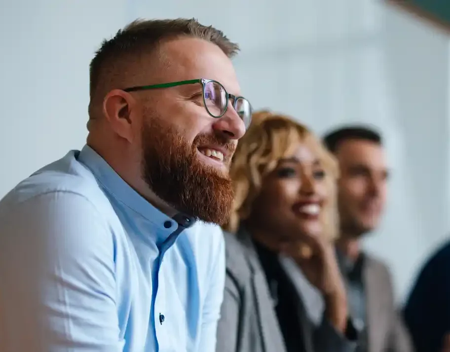 Mortgage broker with beard at a meeting with content writers, smiling inside office setting.