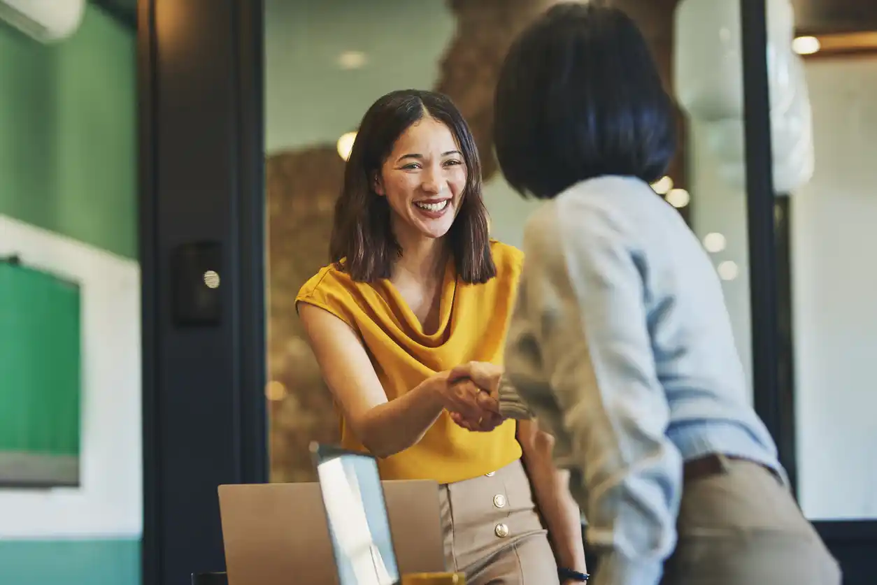 Female content writer in professional setting shaking hands with female finance expert.
