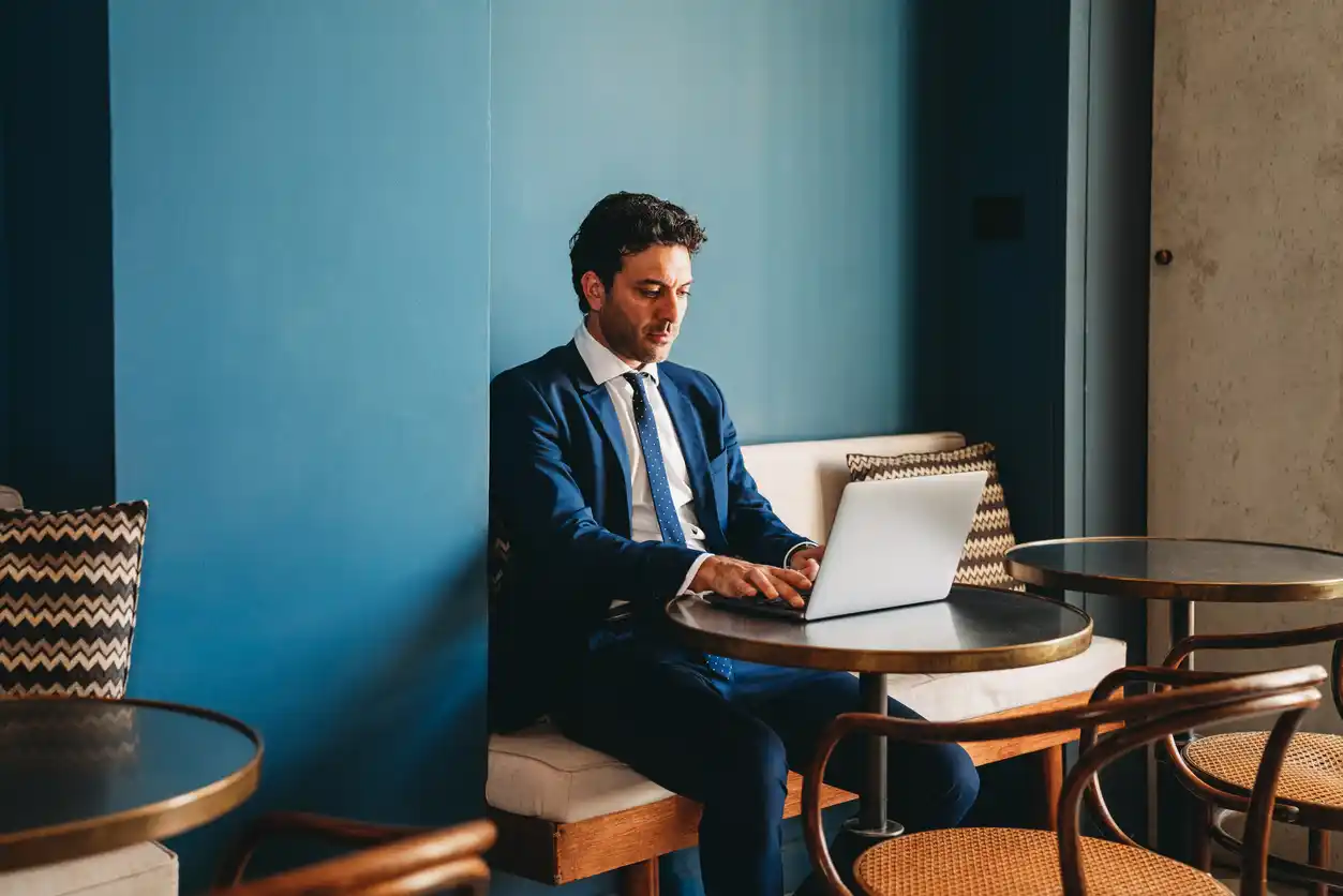 Savvy mortgage broker looking at website content in cafe with blue feature wall behind and empty seats around him.